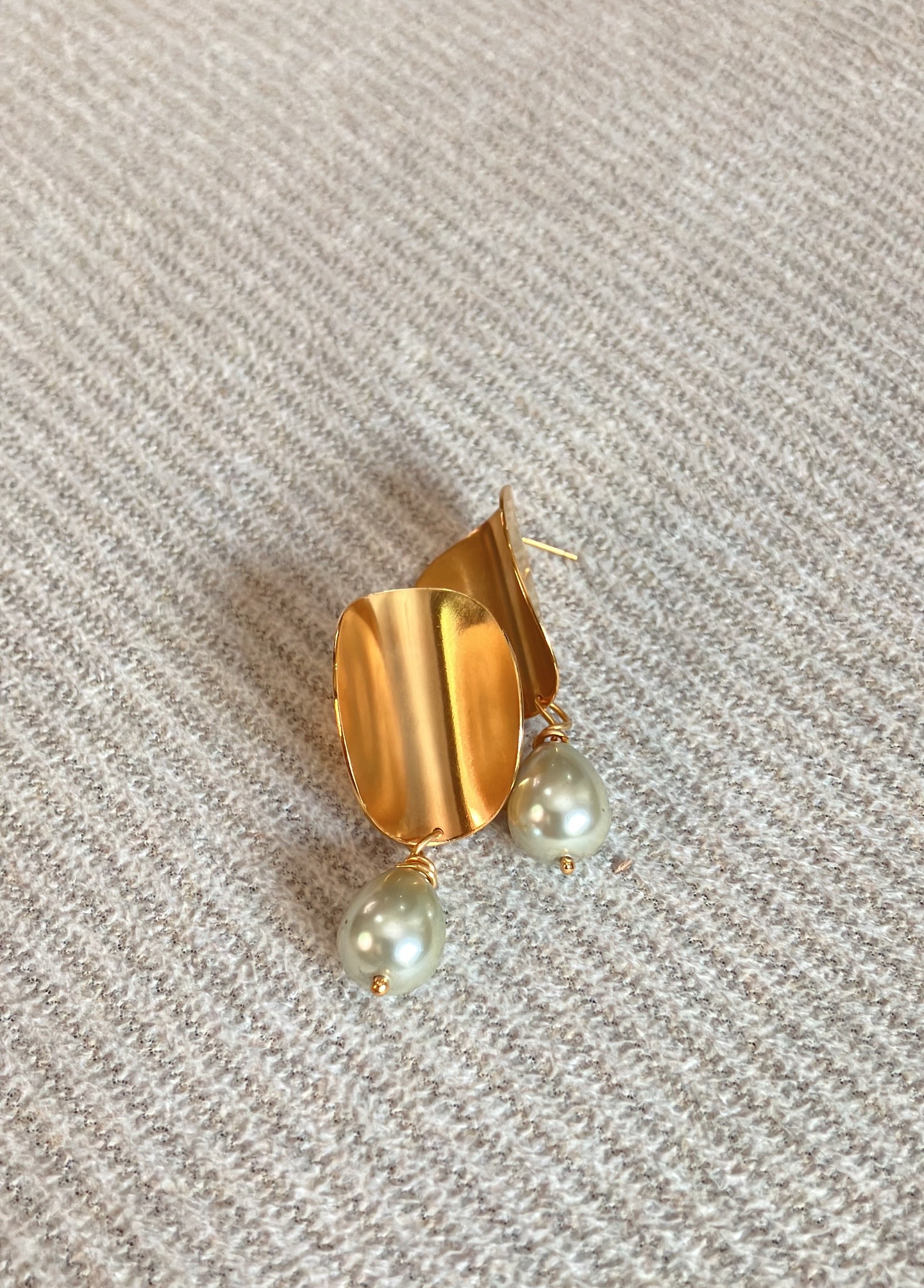 a gold plated medium sized folded circle statement earrings with a creamy colored pearl dangling at the bottom